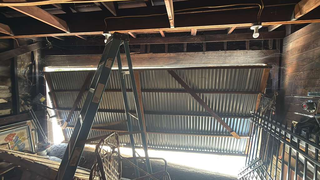 Old garage door off its track inside a wood-framed garage, corrugated metal door sagging off the rails, emergency repair by MSB