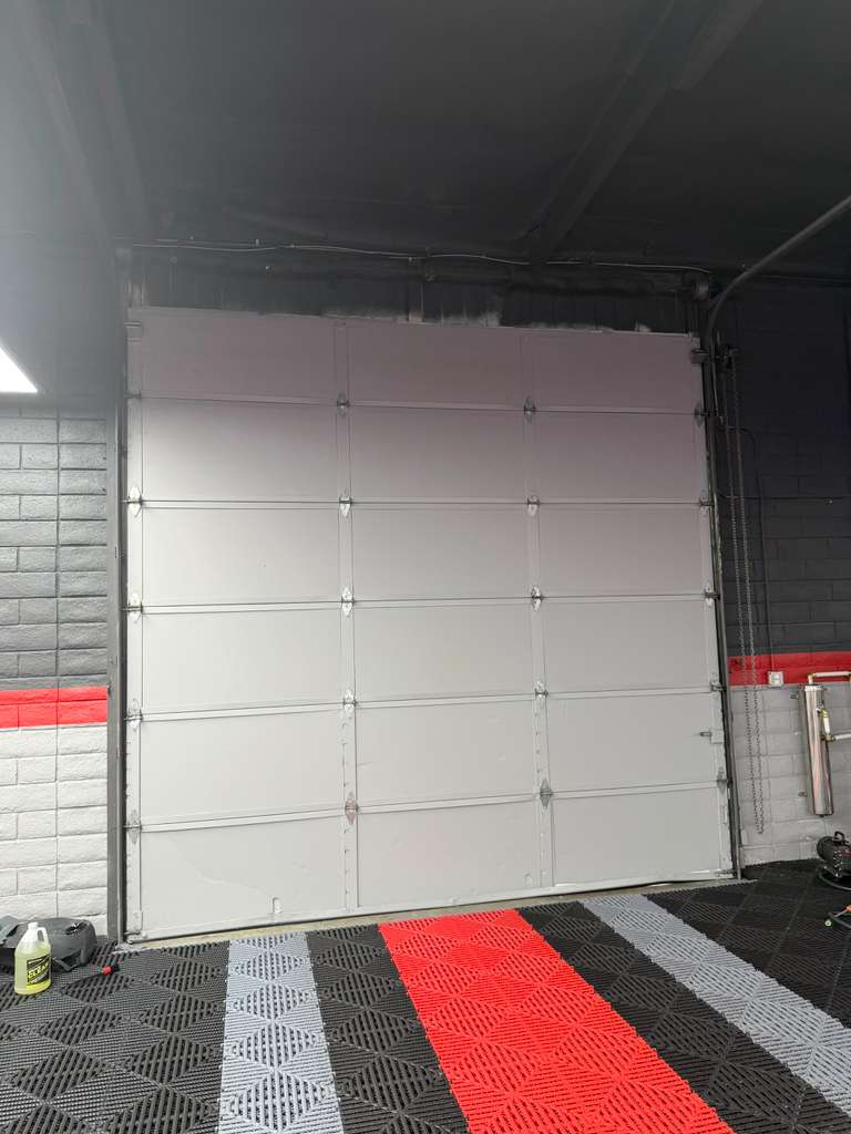 White commercial sectional garage door installed inside a Los Angeles shop with red and black tile flooring