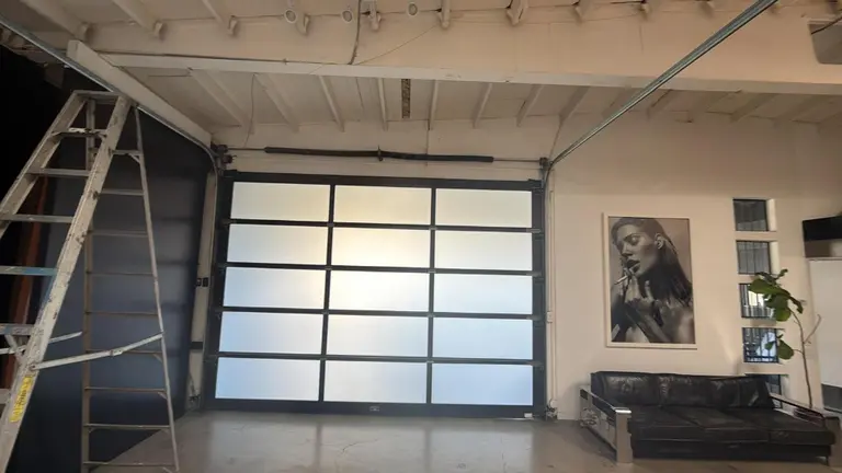 Full-view frosted glass garage door with black aluminum frame installed in modern loft-style commercial space in Los Angeles