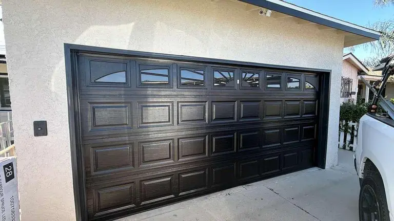Classic raised panel garage door with arched decorative window inserts in traditional brown finish for Los Angeles residential home