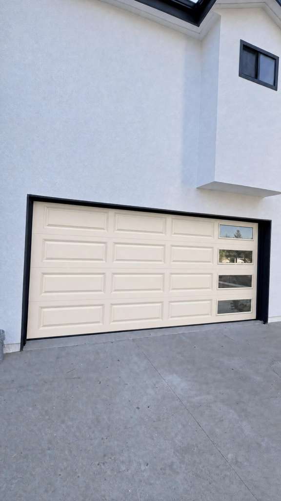New tan raised-panel double-car garage door with side window inserts installed at a modern Los Angeles home