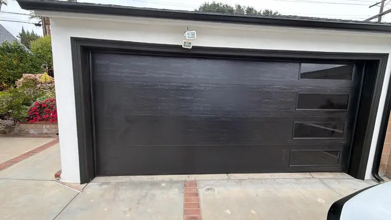 Contemporary black garage door featuring four offset horizontal glass window panels in modern architectural design